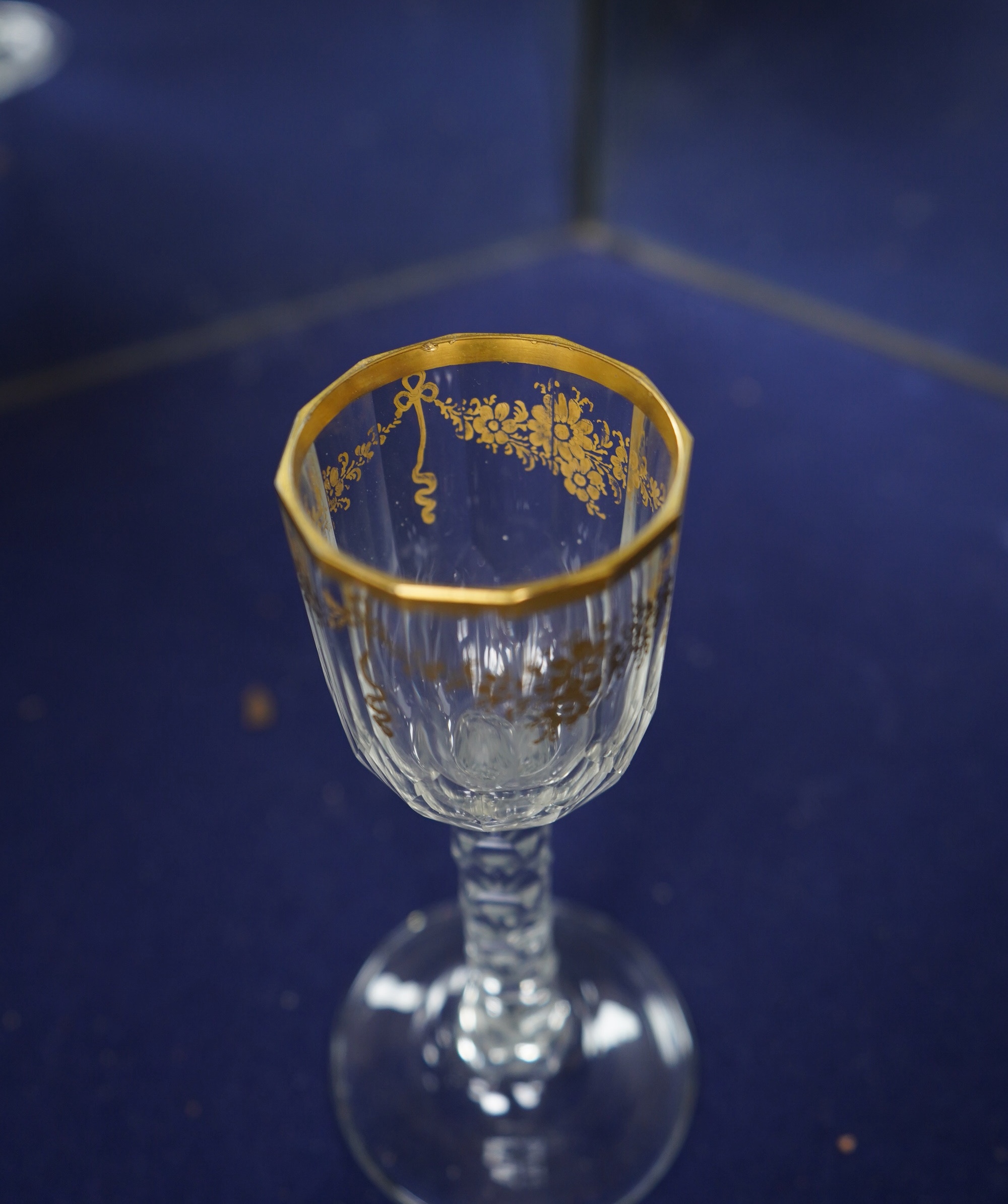 A pair of early 18th century octagonal glasses with gilt floral swagged decoration and facetted stems. Condition - slight wear to gilding otherwise good